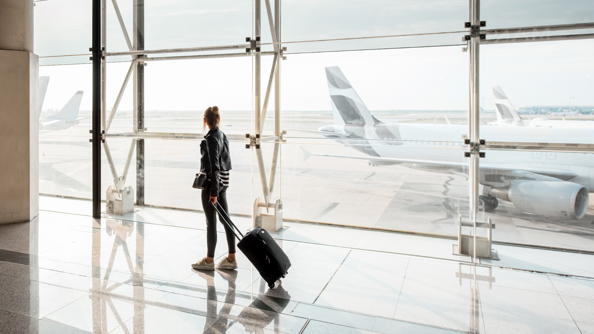 A woman standing in an airport with an airplane seen through the window